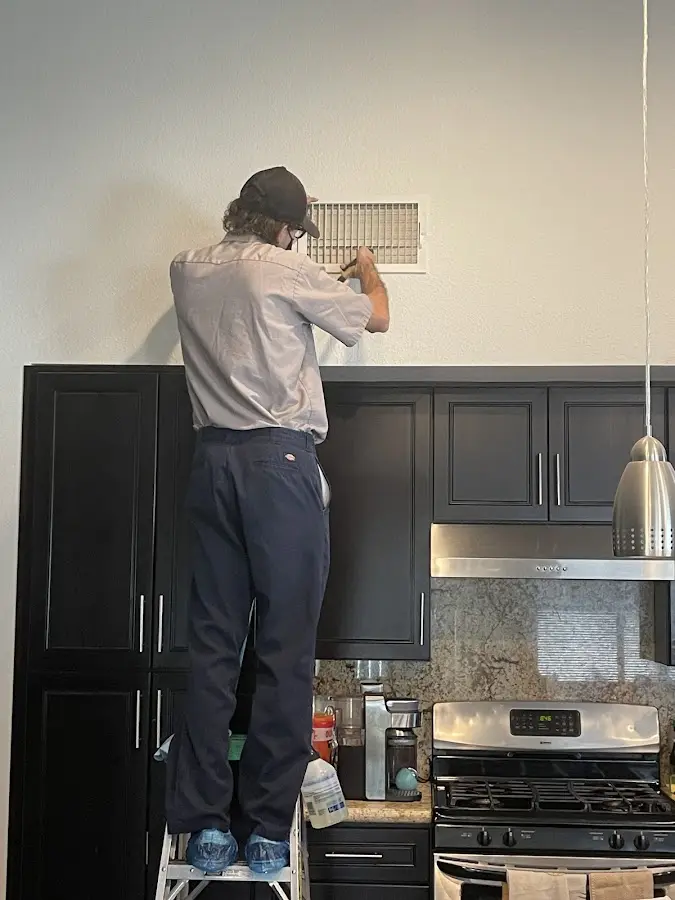 Technician inspecting an air vent during HVAC service in Oak Island